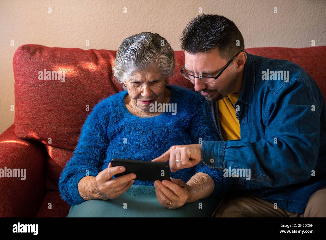 Grand-mère tenant un smartphone pour la vidéo avec son petit-fils assis dans le salon. Deux générations en ligne avec le téléphone sur le canapé à la maison. Elderl Banque D'Images