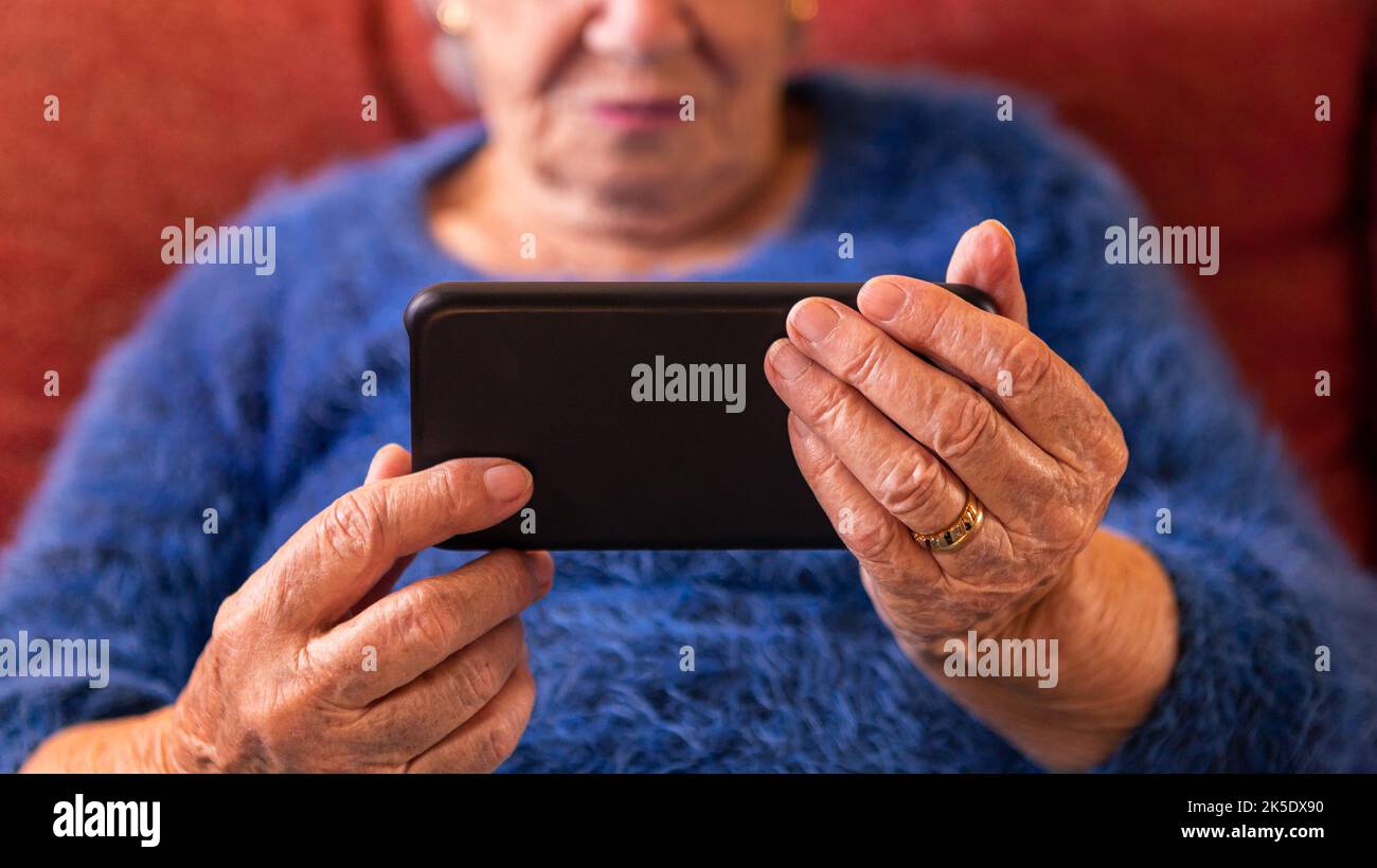 Une vieille femme à la maison utilisant un téléphone portable. Les mains froissées de la grand-mère tient un smartphone. Concept de technologie Banque D'Images
