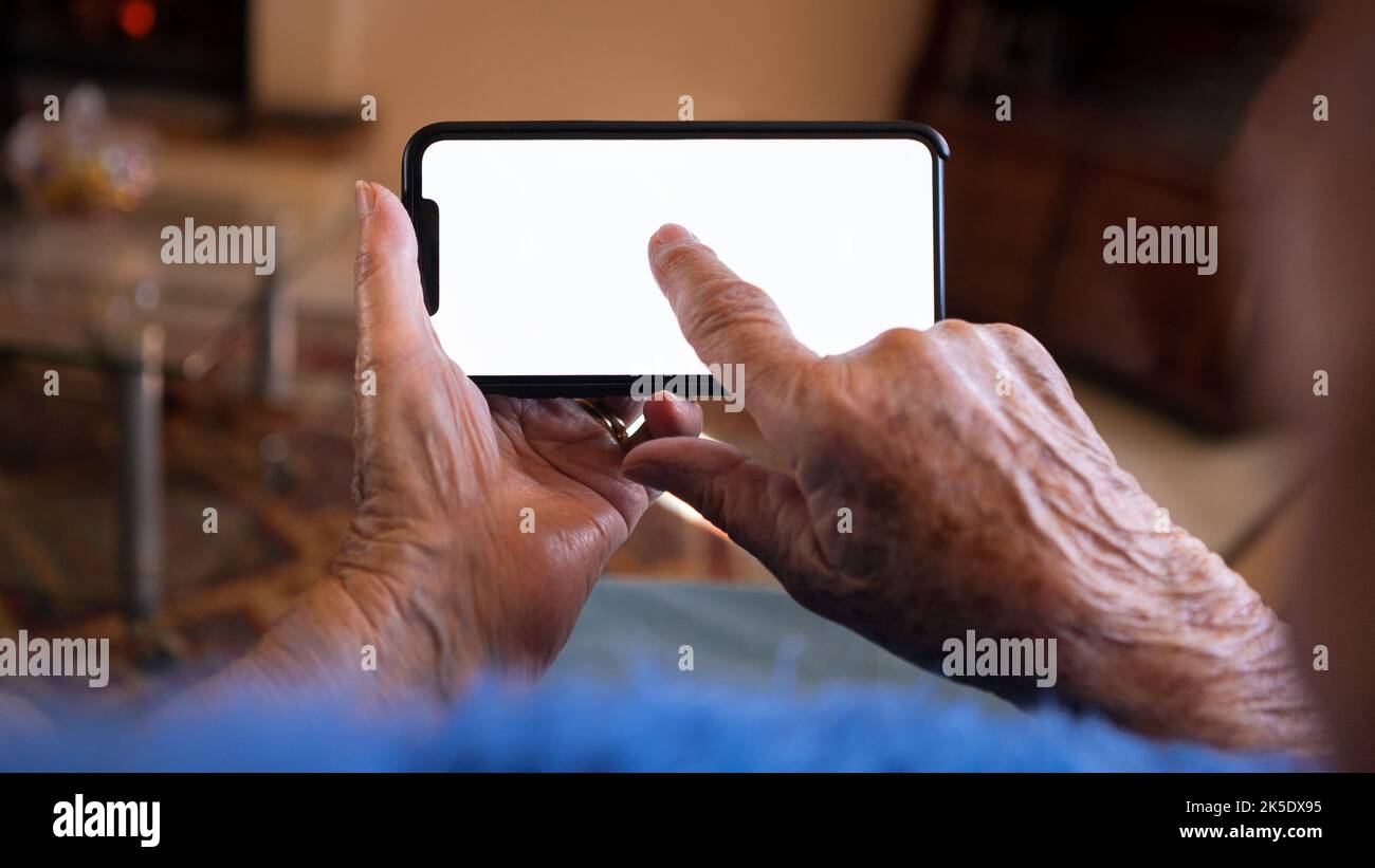 Les mains froissées de la vieille femme tient un smartphone avec écran blanc vide pour votre maquette. Gros plan des mains âgées de grand-mère caucasien montrant blanc Banque D'Images