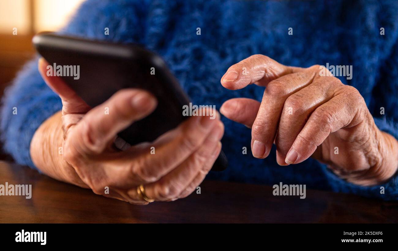 Femme âgée utilisant un téléphone portable tout en étant assise dans le salon à la maison. Grand-mère tient un smartphone. Ancien grand-mère utilisant un téléphone. Concept de te Banque D'Images