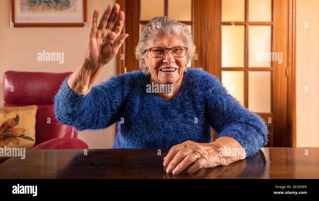 Bonne vieille femme avec un sourire sur son visage main tombée en salutation. Caucasien 90s grand-mère dans la salle de séjour à la maison. Grand-mère bonjour et accueil des invités Banque D'Images