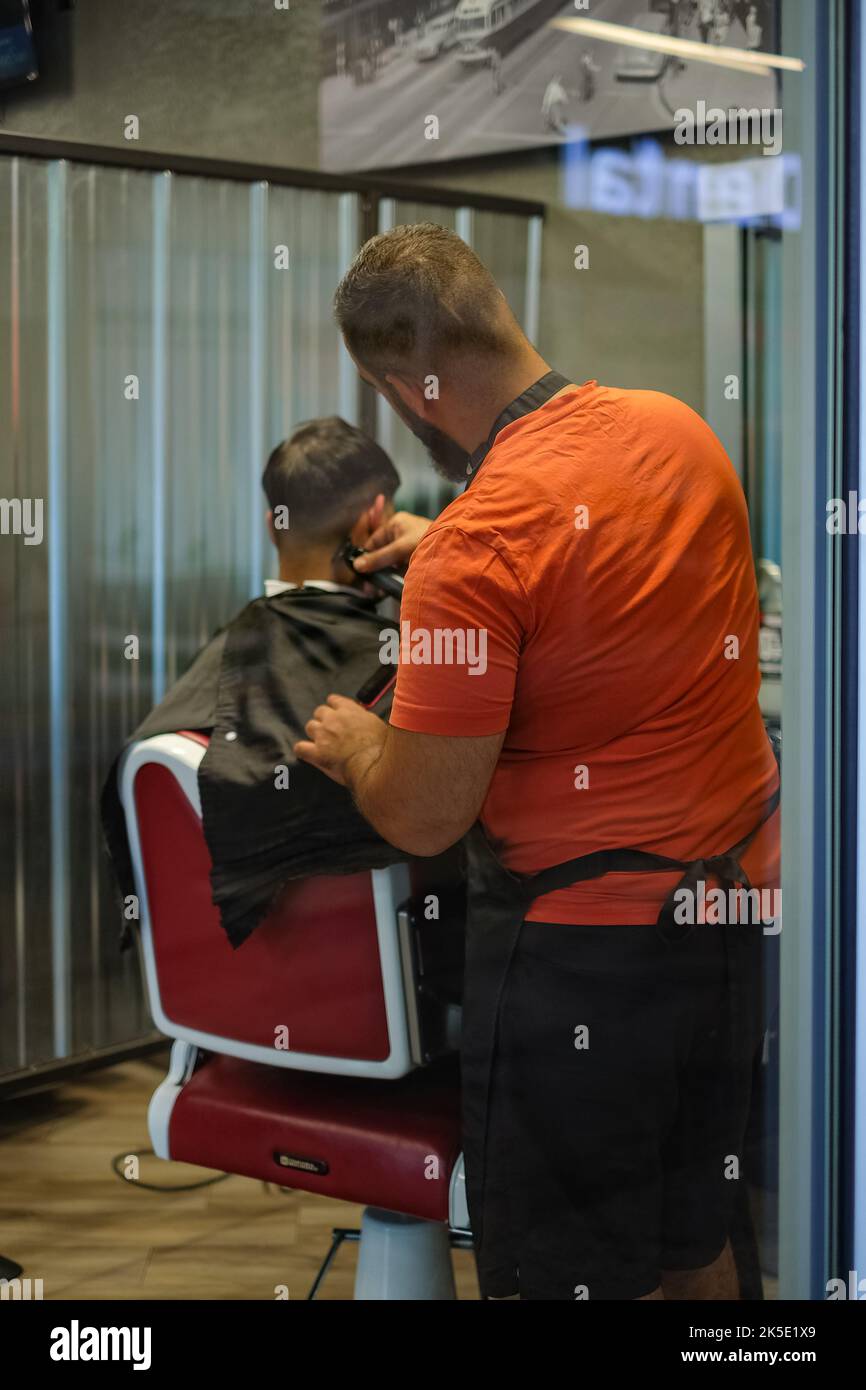 Coiffeur masculin faisant une coupe de cheveux pour un jeune homme au salon de coiffure. Il est debout derrière le client peignant les cheveux. Vue du processus de coupe des cheveux de l'homme c Banque D'Images