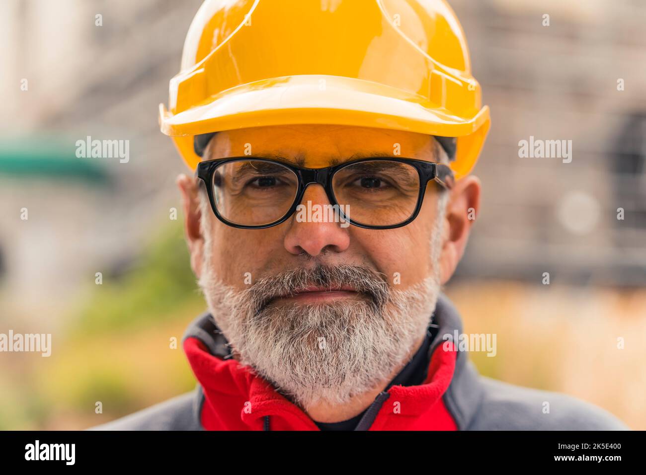 Gros plan portrait du visage sérieux de l'homme caucasien avec des cheveux gris et des lunettes à monture noire portant un casque de protection jaune. Ingénierie et architecture. Photo de haute qualité Banque D'Images