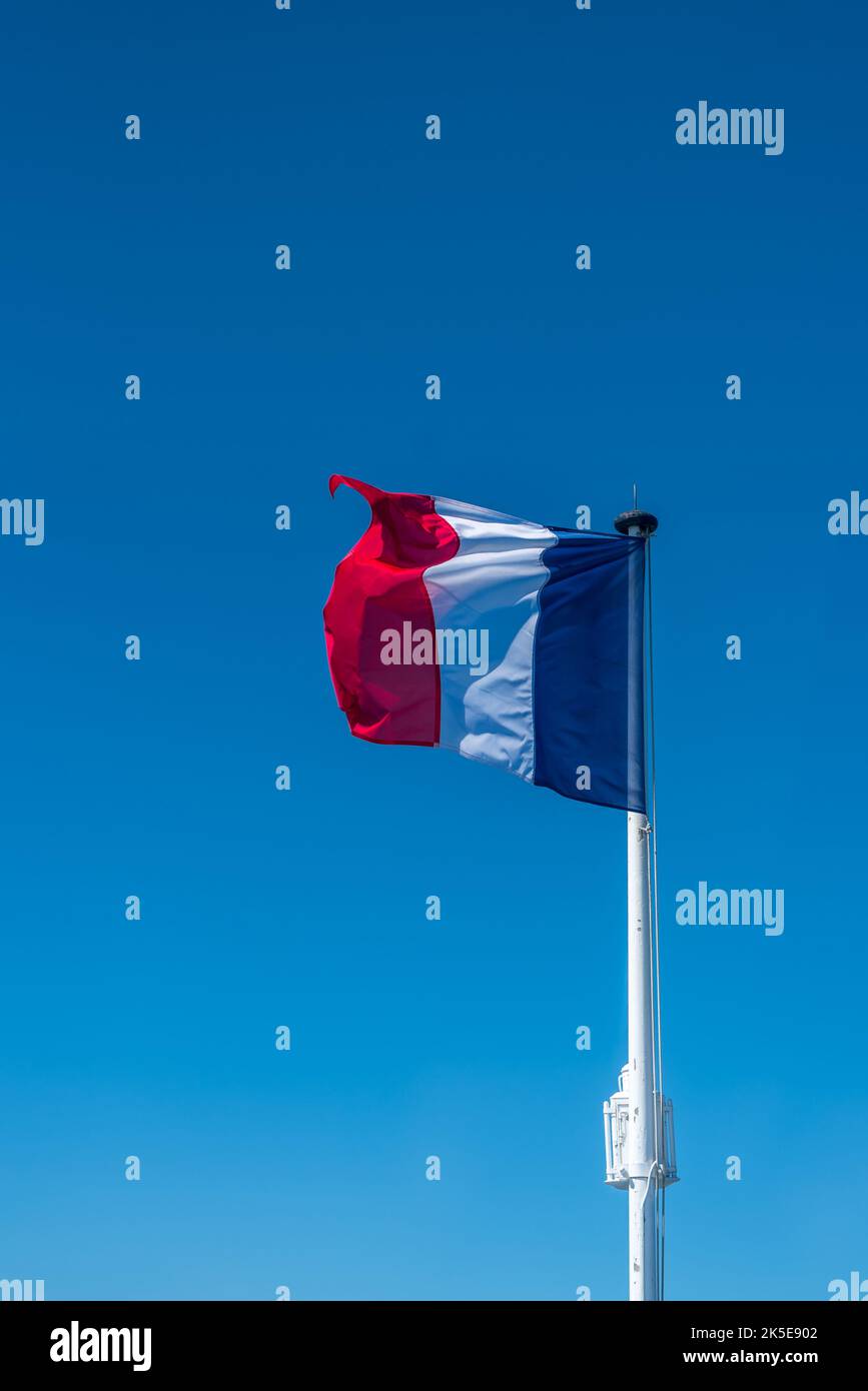 Drapeau français sur le mât au-dessus d'un ciel bleu. Banque D'Images