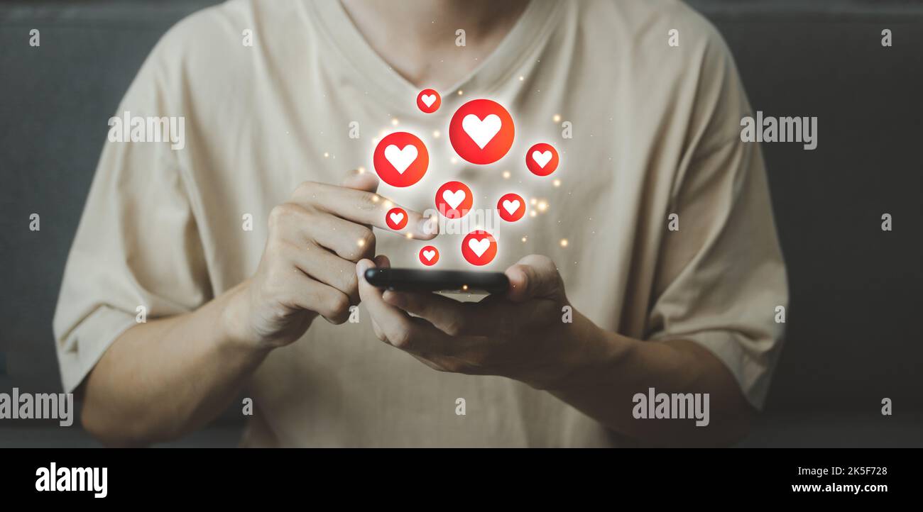 Chat et notification sur smartphone avec l'icône de réseau social emoji à cœur rouge virtuel. Homme utilisant un smartphone en vacances avec hologramme. Médias sociaux et d Banque D'Images