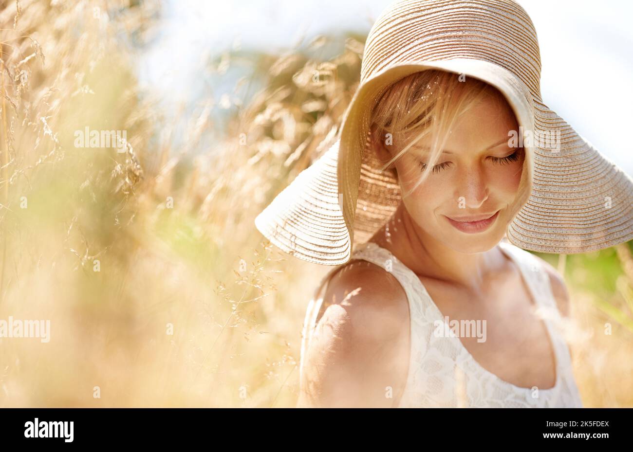 C'est un jour si beau... une belle jeune femme dans un chapeau de soleil marchant à travers l'herbe haute. Banque D'Images