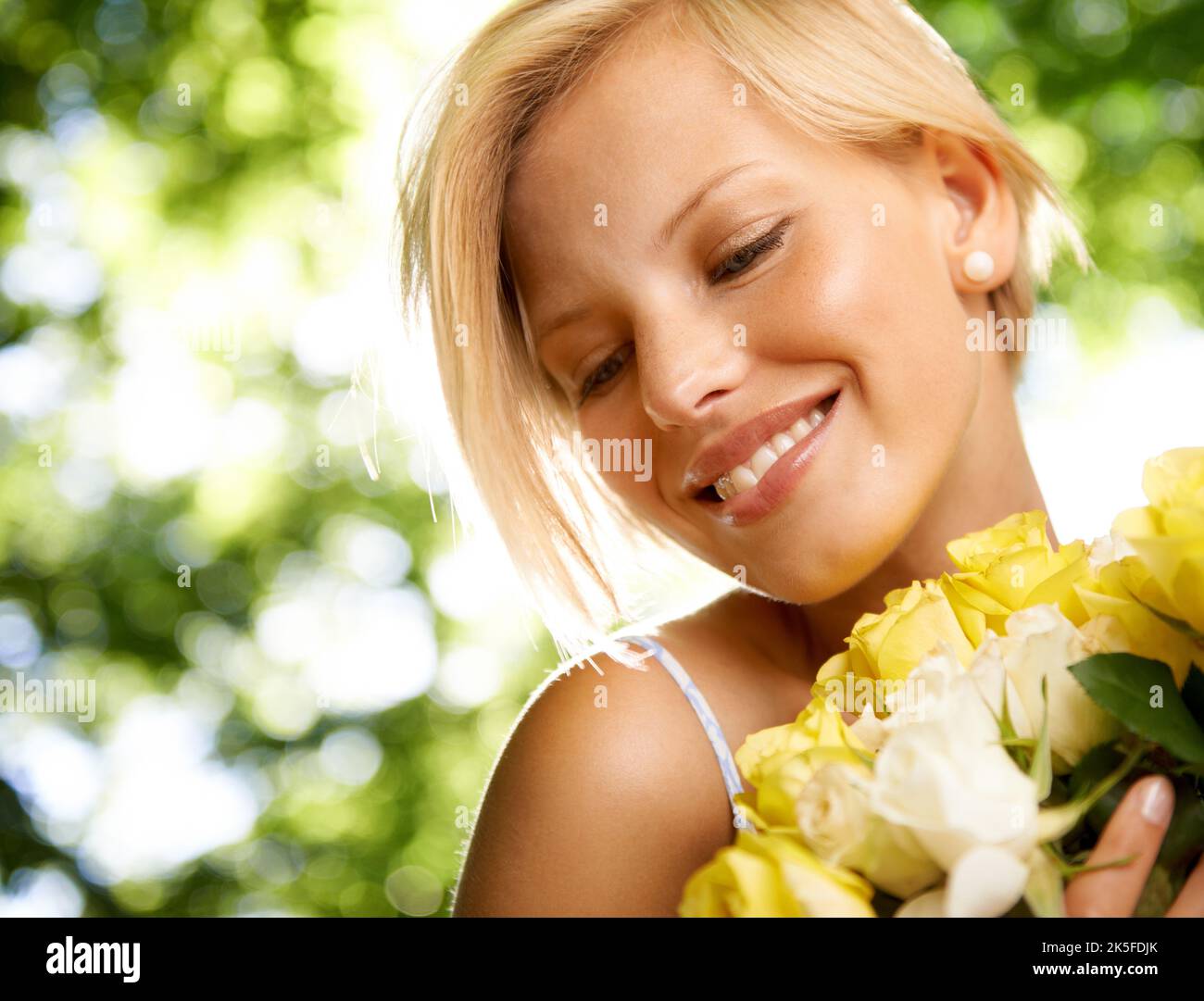 Elle rend tout plus agréable. Une jeune femme souriante debout dehors tenant un bouquet de jaune. Banque D'Images