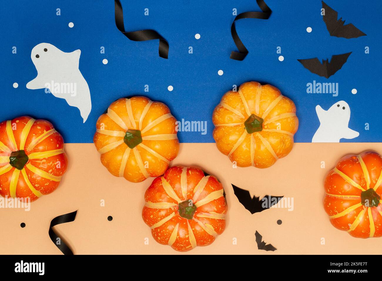 Halloween concept, sourire effrayant citrouilles avec fantôme et batte noire sur fond bleu et crème. Banque D'Images