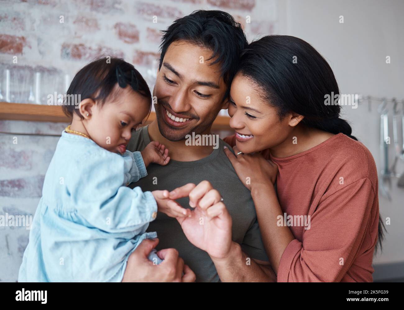 Famille avec le syndrome de Down bébé, parents heureux dans la cuisine maison ensemble et garde de jeunes enfants. Père indien tenant un enfant mignon, mère asiatique sourire avec Banque D'Images