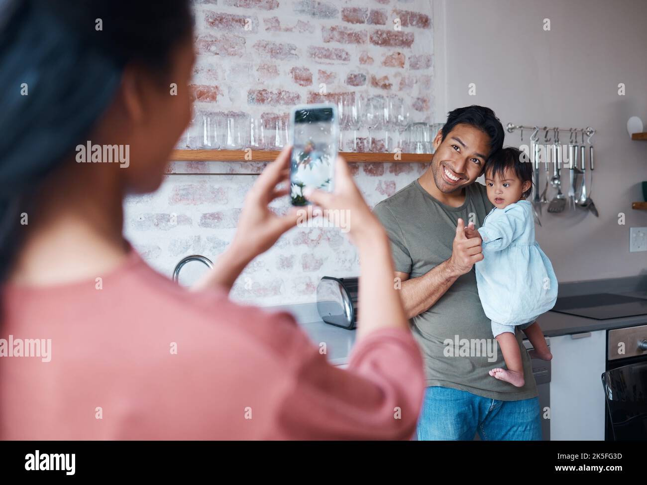 Famille, soins et mère avec téléphone pour la photo de père et de bébé avec le syndrome de Down dans le salon de leur maison. Maman prenant une photo d'un heureux Banque D'Images