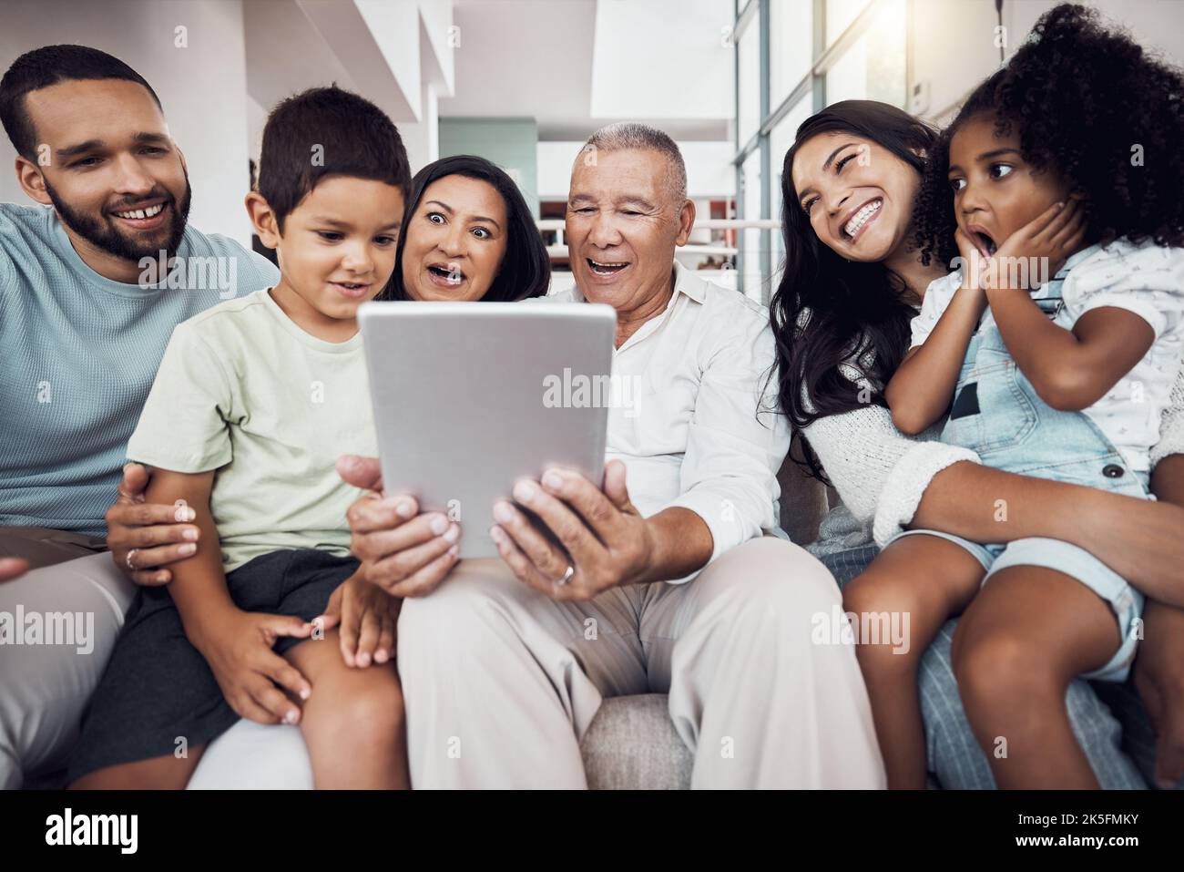 Famille, maison et divertissement avec une tablette pour diffuser un film, un abonnement vidéo ou un spectacle en ligne. Amour, surprise et bonne famille sur un canapé sourire Banque D'Images