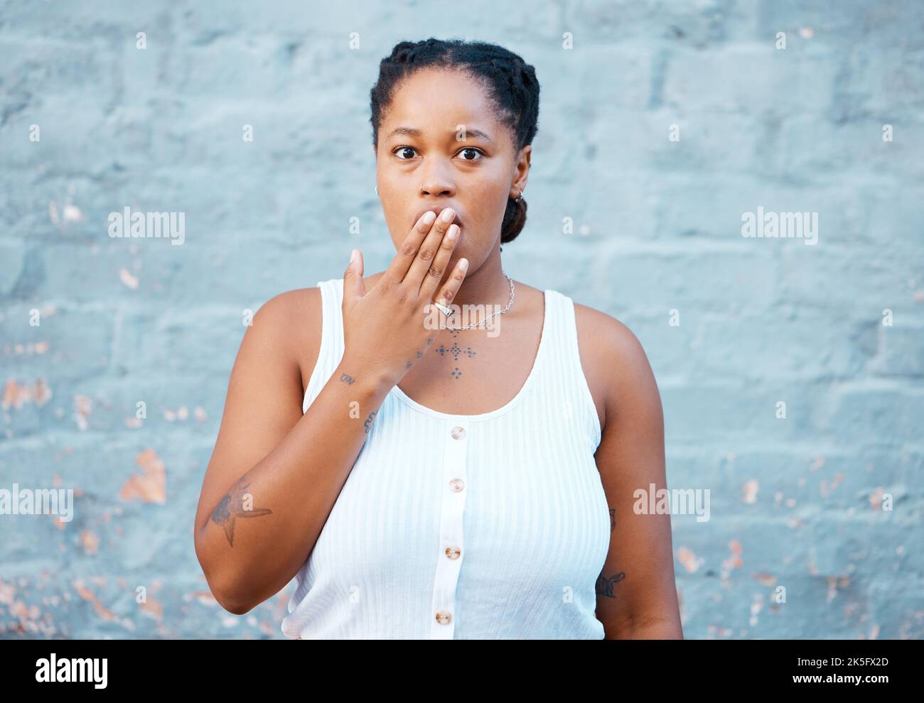 Femme noire choquée, main et souci dans le silence pour le secret contre un fond de mur. Portrait d'une femme afro-américaine qui couvre la bouche en question Banque D'Images
