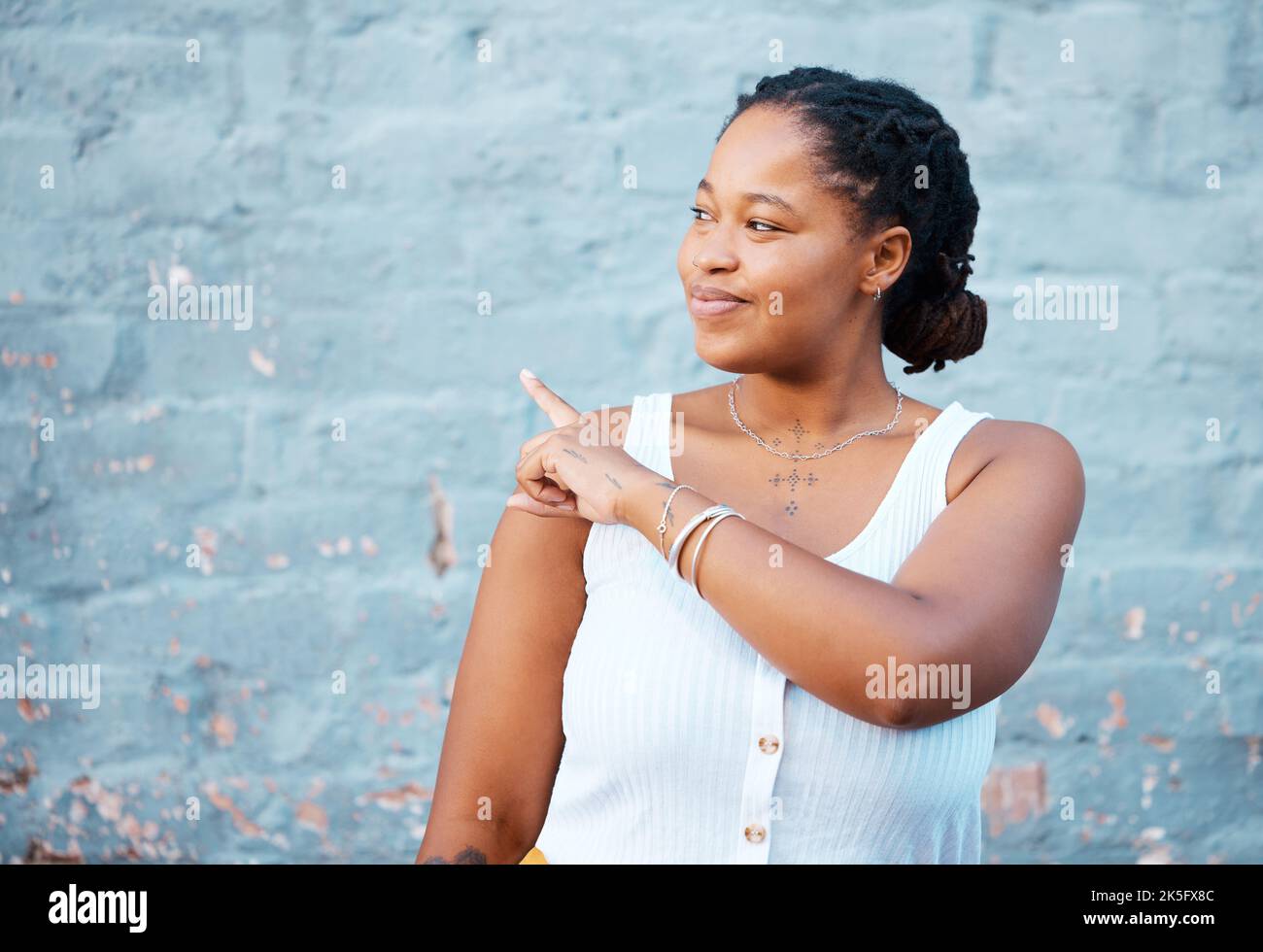 Femme noire pointant le doigt pour montrer la publicité, la promotion ou la maquette commerciale, espace de marketing sur le mur bleu extérieur gen z, style de vie des jeunes. Fille africaine Banque D'Images