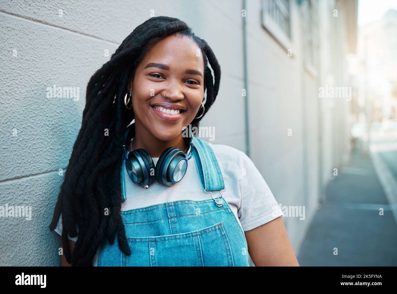 Femme noire, sourire et heureuse étudiante en milieu urbain jeune fille dans la rue de la ville souriant et se penchait contre un mur à l'extérieur sur le trajet à l'université. Portrait d'un Banque D'Images