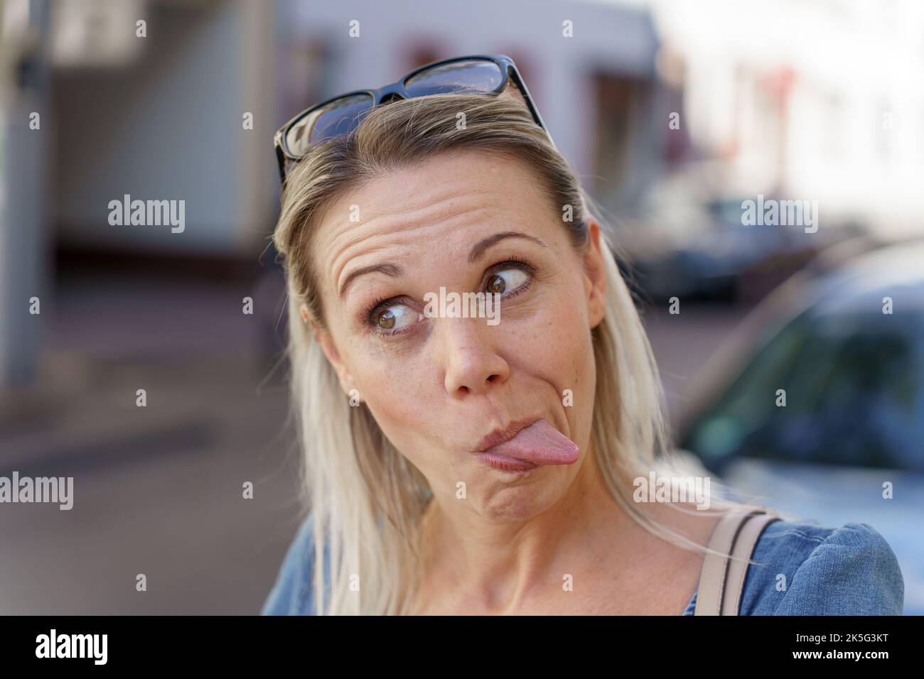 Femme blonde tendance tirant un visage drôle en collant sa langue à la caméra comme elle regarde loin Banque D'Images