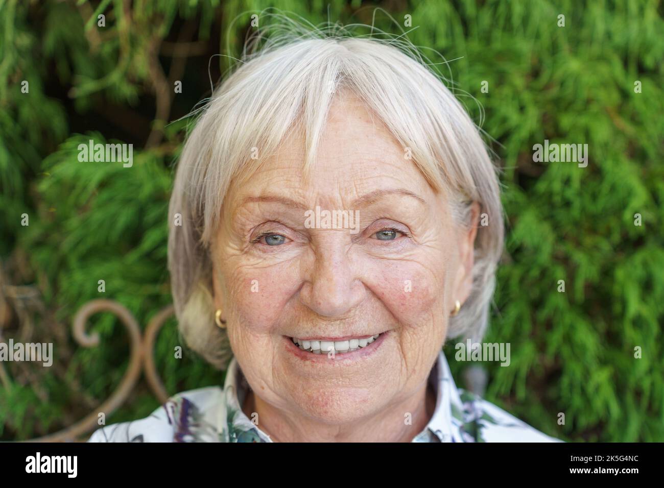 Portrait en tête d'une femme sénior attirante donnant à l'appareil photo un sourire chaleureux et enrayant à l'extérieur dans un jardin Banque D'Images
