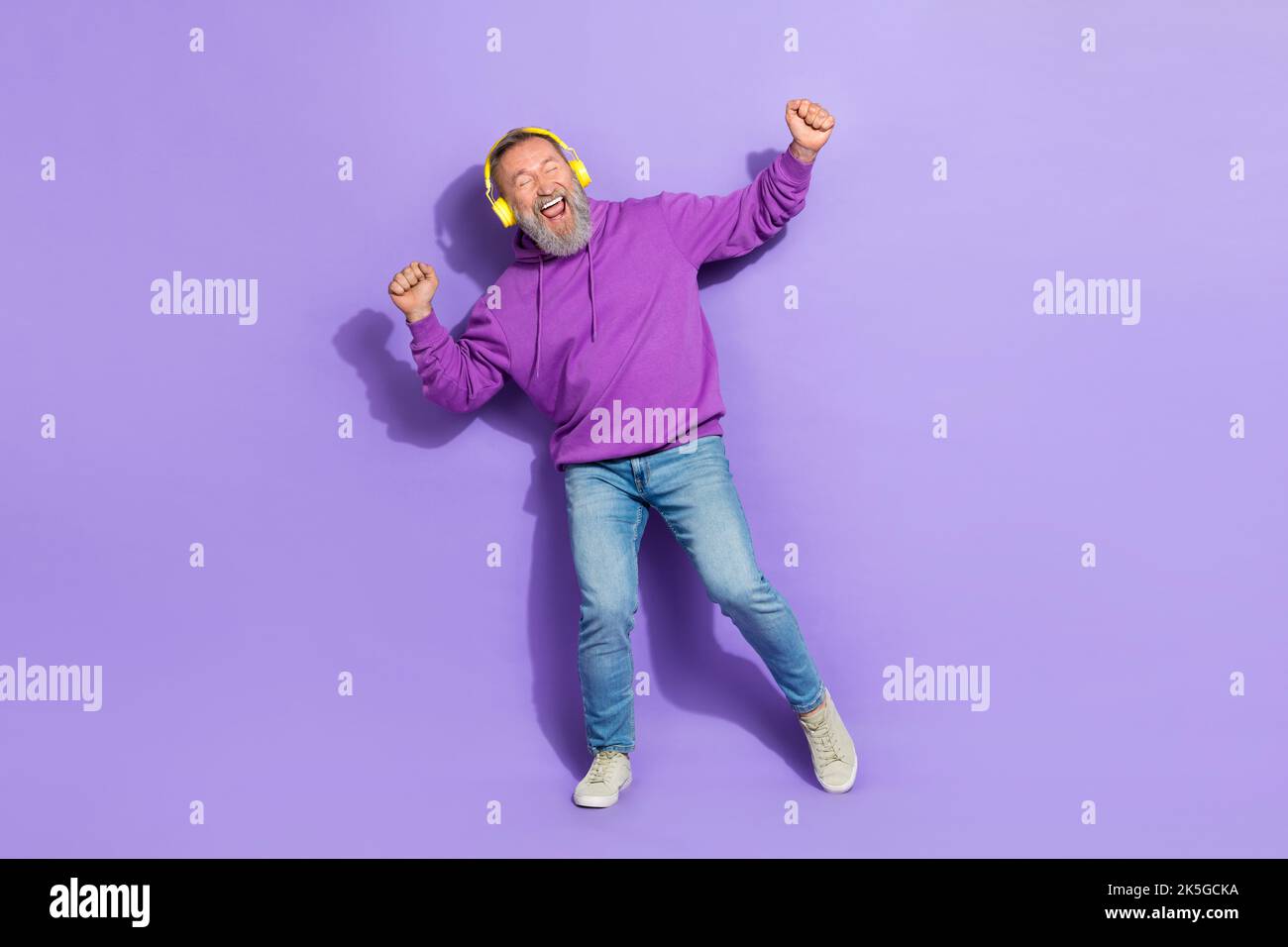 Photo de l'homme sain et optimiste senior porter un casque à capuche violet dansant des chansons préférées pistes isolées sur fond violet Banque D'Images