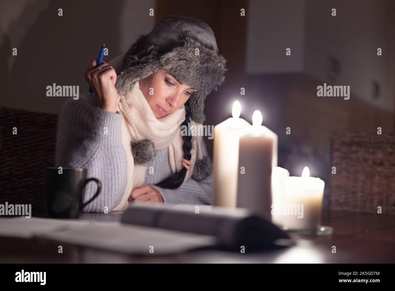 Elle est assise dans un chapeau d'hiver à un hoem qui fait de la paperasse sous les lumières des bougies alors que la Russie coupe ses approvisionnements en gaz et que l'Europe souffre d'une crise énergétique. Banque D'Images