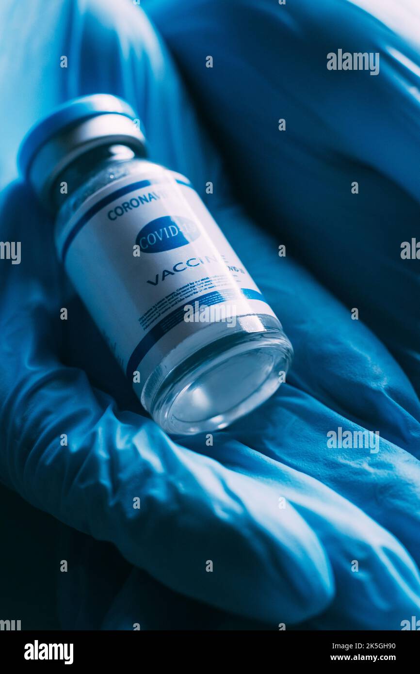 Vaccin Covid-19. Anticorps du coronavirus. Immunisation en cas de pandémie. Traitement médical. Flacon de dose avec étiquette dans les mains du médecin en protection bleue Banque D'Images