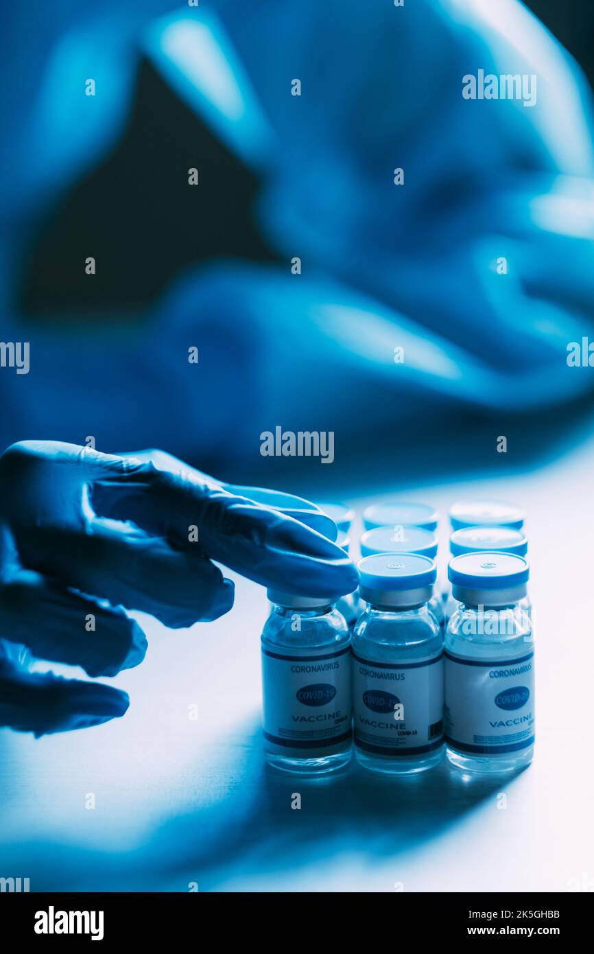 Étude de vaccin. Immunisation Covid-19. Recherche pharmaceutique. Essai clinique. Les mains des scientifiques dans des gants de protection bleus epi test flacons de dose flacon Banque D'Images