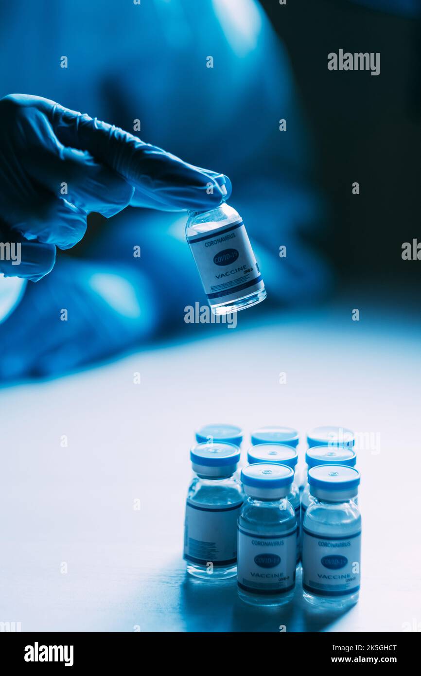 Recherche sur les vaccins. Immunisation contre le coronavirus. Arrêter la pandémie. Vaccin contre la grippe. Main scientifique dans un gant de protection bleu epi test flacons de dose flacons sur bleu foncé bl Banque D'Images