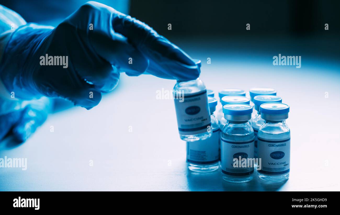 Analyse des vaccins. Immunisation Covid-19. Recherche en laboratoire. Vaccin contre la grippe. Main du médecin dans un gant de protection bleu epi test flacons de dose flacons sur BL foncé Banque D'Images