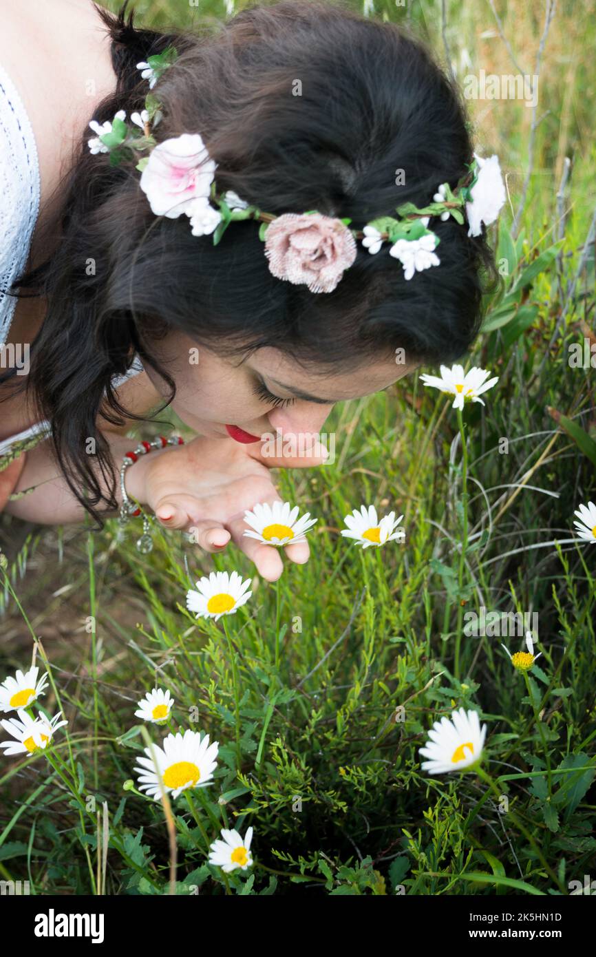 Jeune femme portant une coiffe florale qui sent des pâquerettes dans un pré, en Espagne Banque D'Images