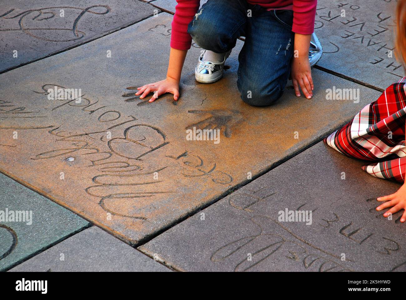 Une femme prend la taille de ses mains dans les empreintes de la star de cinéma Marylin Monroe dans la cour en ciment et la plaza du théâtre chinois de Grauman à Hollywood Banque D'Images