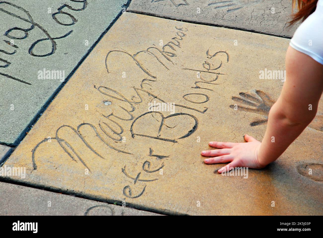 Une jeune femme met ses mains dans les empreintes de la star de cinéma Marilyn Monroe, dans la célèbre cour du théâtre chinois, à Hollywood Banque D'Images