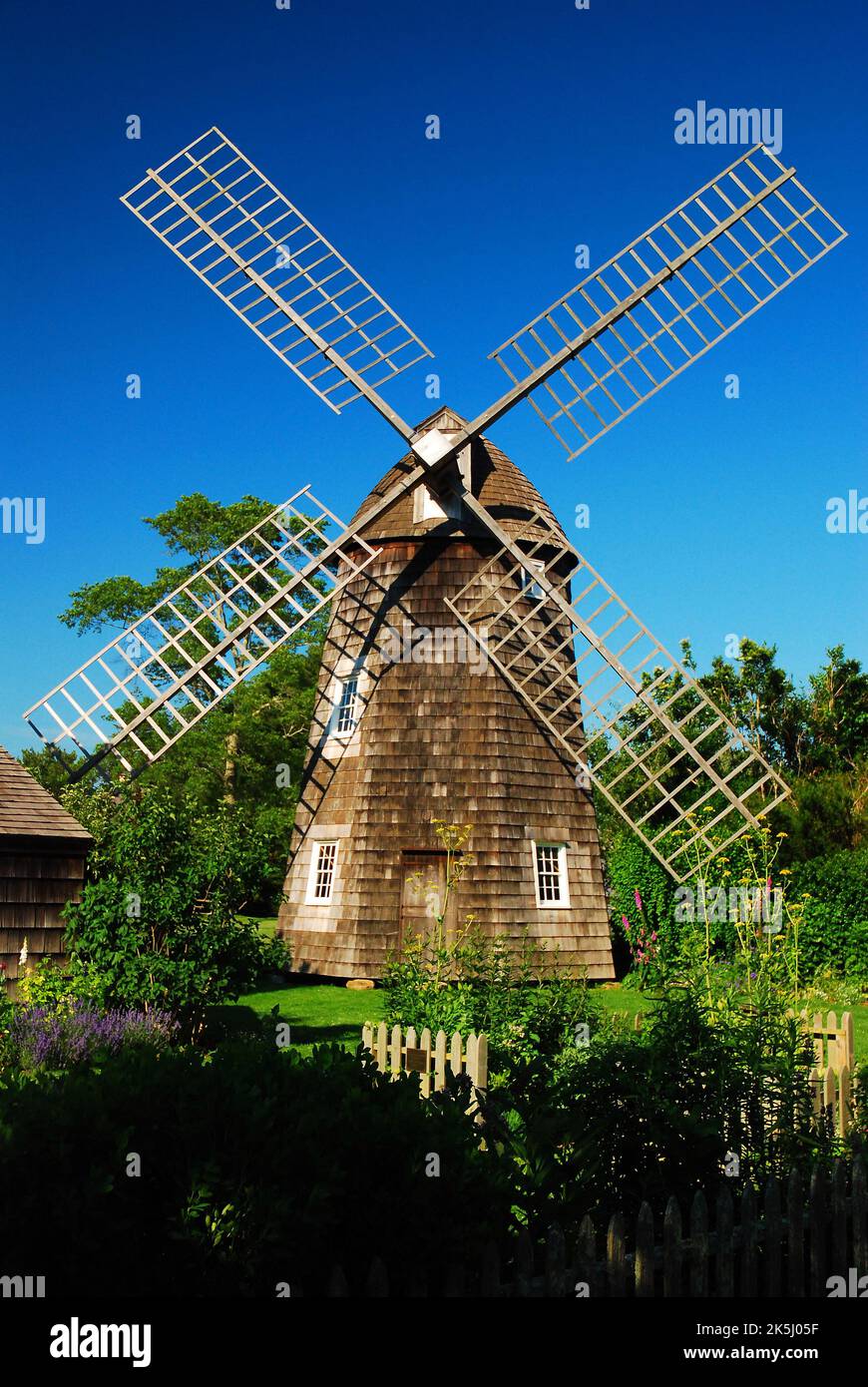 Un moulin à vent historique en bois se trouve au centre d'un jardin d'été fleuri dans un musée dédié à la vie rurale coloniale Banque D'Images