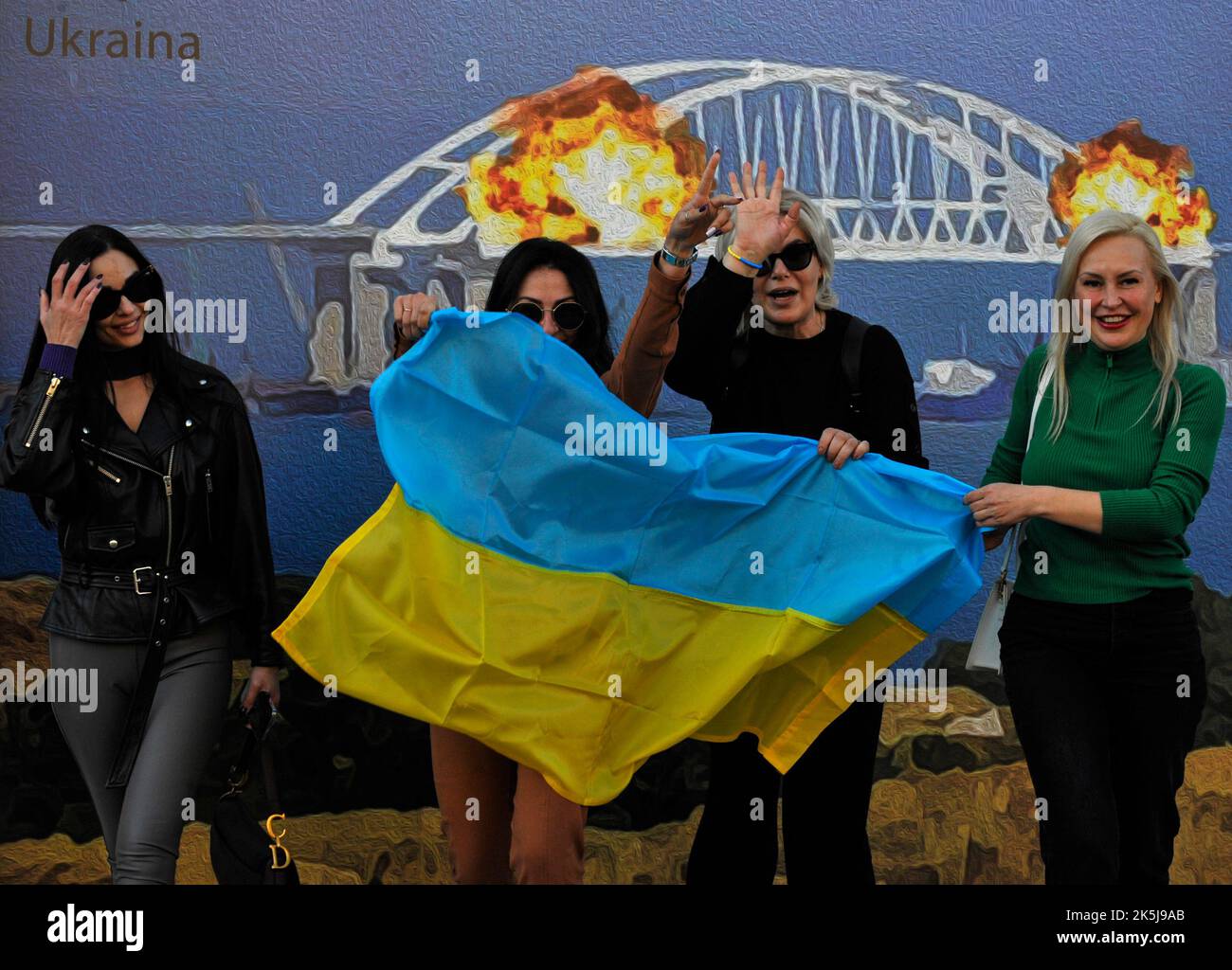 Kiev, Ukraine. 8th octobre 2022. Les femmes arborent le drapeau ukrainien pour prendre une photo sur l'arrière-plan de la disposition du timbre qui représente le pont de Kerch en feu. Sur 8 octobre, sur le pont de Crimée reliant la Russie à la péninsule occupée par elle, après l'explosion, un incendie fort a éclaté. (Credit image: © Sergei Chuzavkov/SOPA Images via ZUMA Press Wire) Banque D'Images