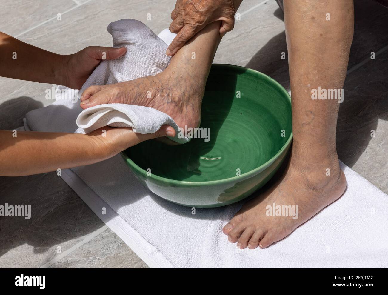 Le personnel soignant féminin essuie les pieds de la femme âgée avec une serviette. Banque D'Images