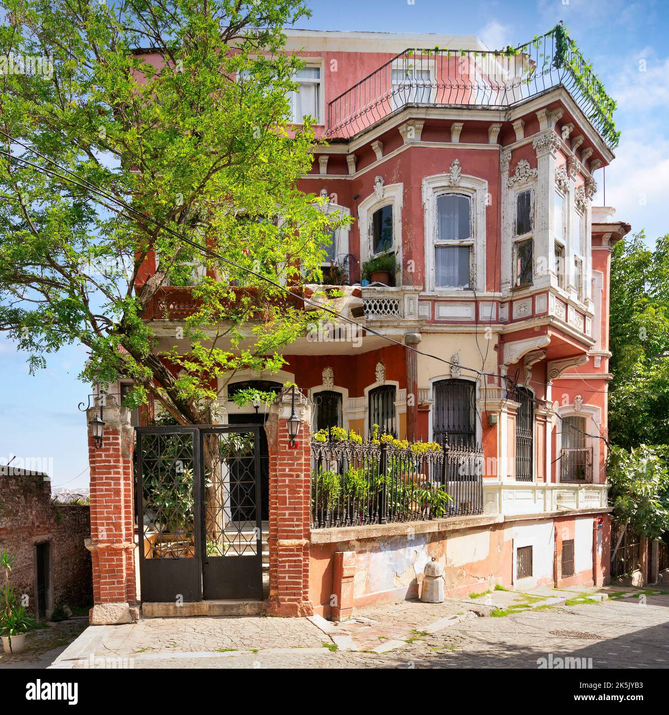 Façade extérieure de vieux bâtiment résidentiel rouge, avec fenêtres en fer forgé, balcons, et arbres verts, quartier Balat, Istanbul, Turquie Banque D'Images
