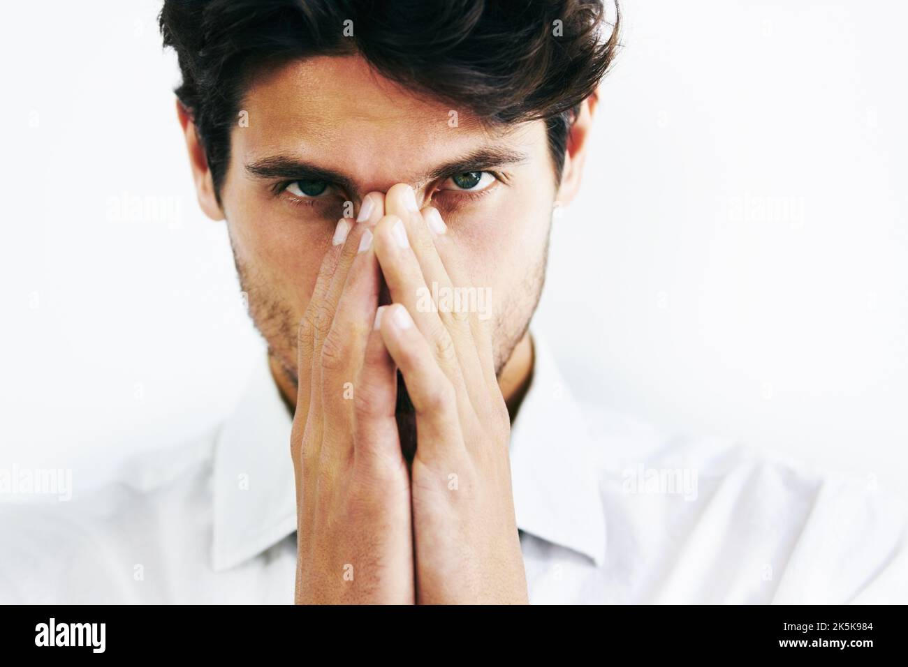 Un look redoutable. Gros plan court iamge d'un homme couvrant son nez et sa bouche avec ses mains regardant la caméra. Banque D'Images