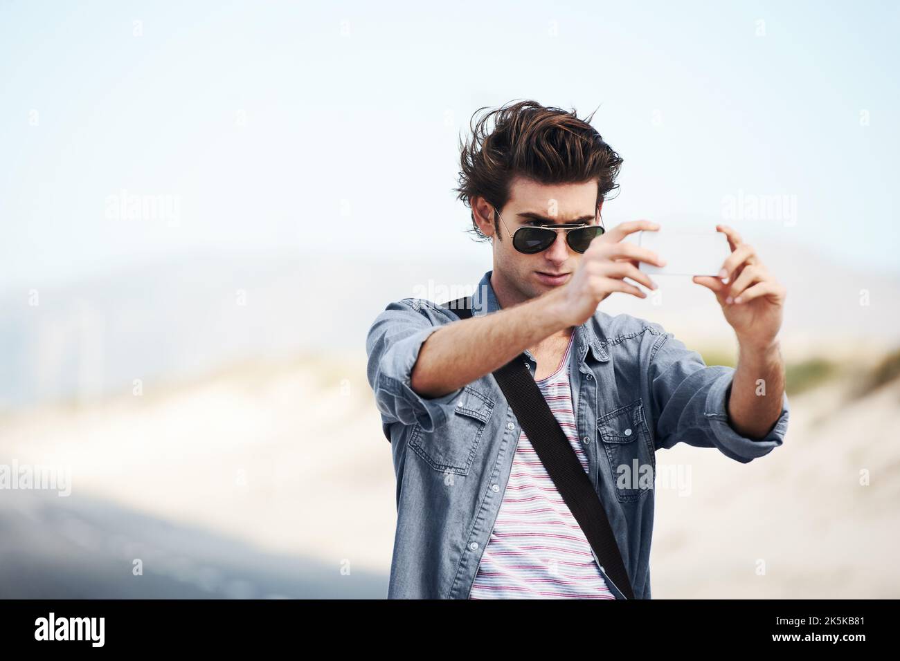 Préserver quelques souvenirs de mon voyage. Jeune homme branché debout sur la route et prenant une photo sur son téléphone. Banque D'Images