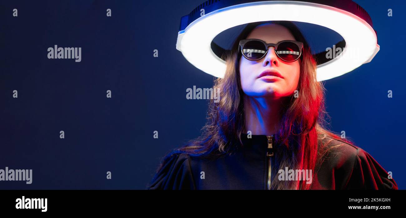 Femme cyberpunk. Bannière futuriste. Technologie quantique. Cyborg femelle au néon rouge dans des lunettes de soleil avec halo de cercle de LED blanc luminescent isolé dans l'obscurité Banque D'Images