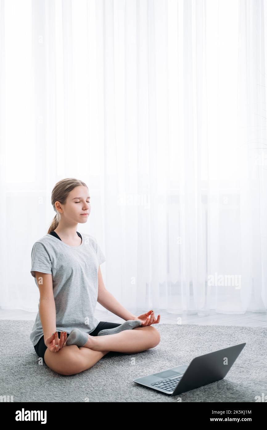 yoga en ligne enfants à la maison méditation fille avec ordinateur portable Banque D'Images