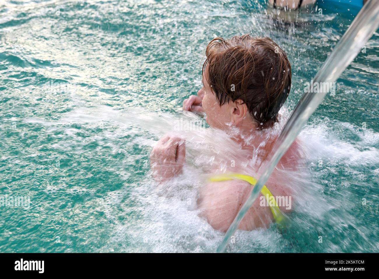 Femme sénior sous le jet d'eau dans la piscine en été Banque D'Images