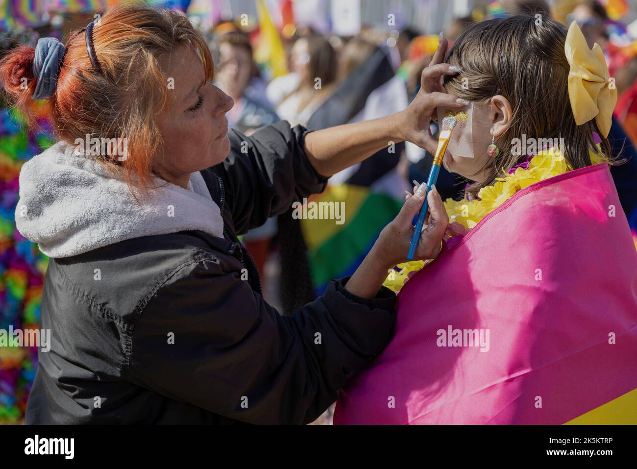 Une femme ayant un coeur brillant peint sur sa joue par un peintre du visage lors d'un événement de fierté gay. Banque D'Images