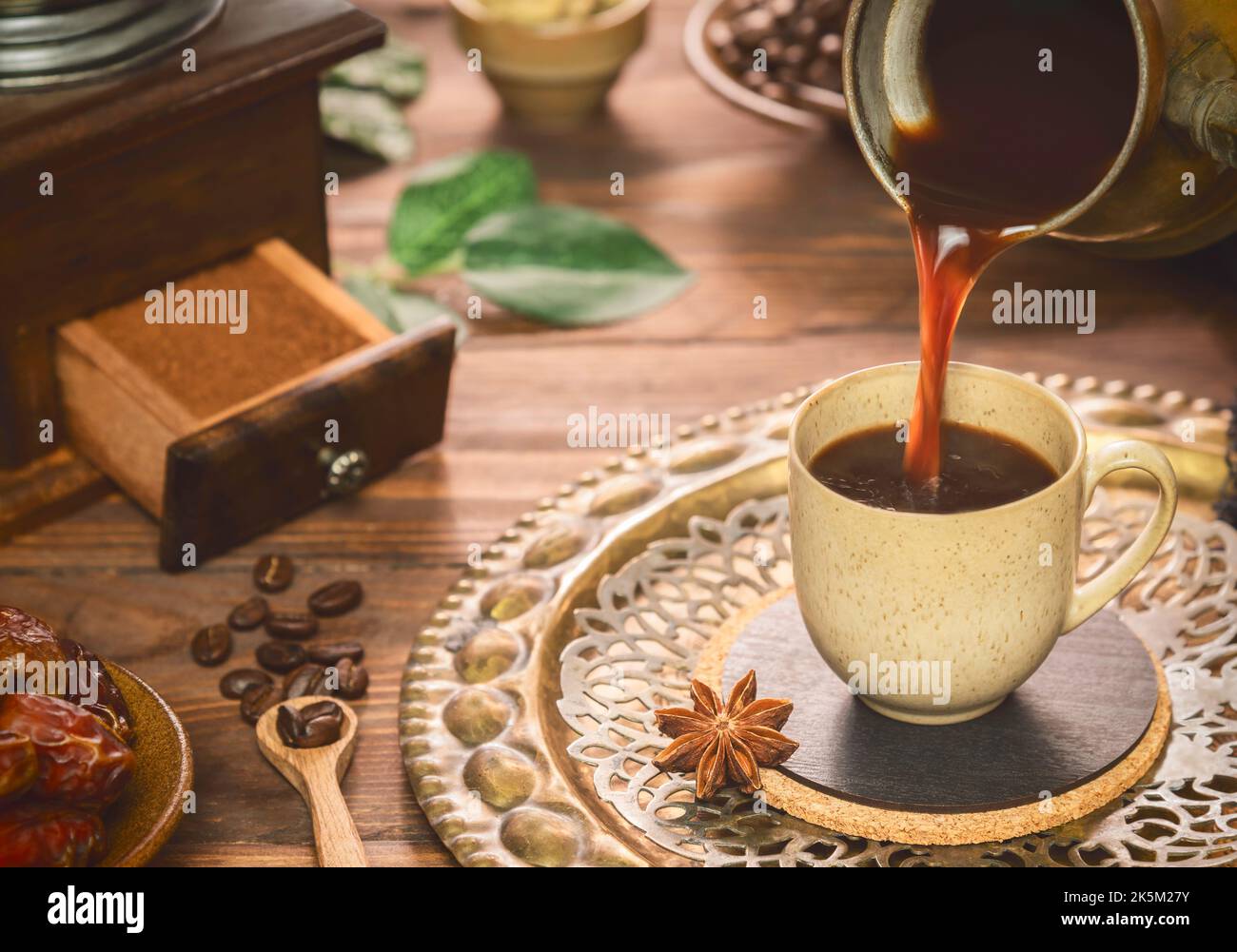 Verser le café turc dans la tasse. Tasse de café placée avec des grains de café rôtis, des dattes fraîches et du café moulu sur fond de bois rustique. Banque D'Images