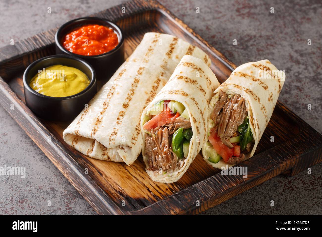 Nourriture traditionnelle arabe sandwich roulé Shawarma avec sauce et légumes sur le panneau en bois de la table. Horizontale Banque D'Images