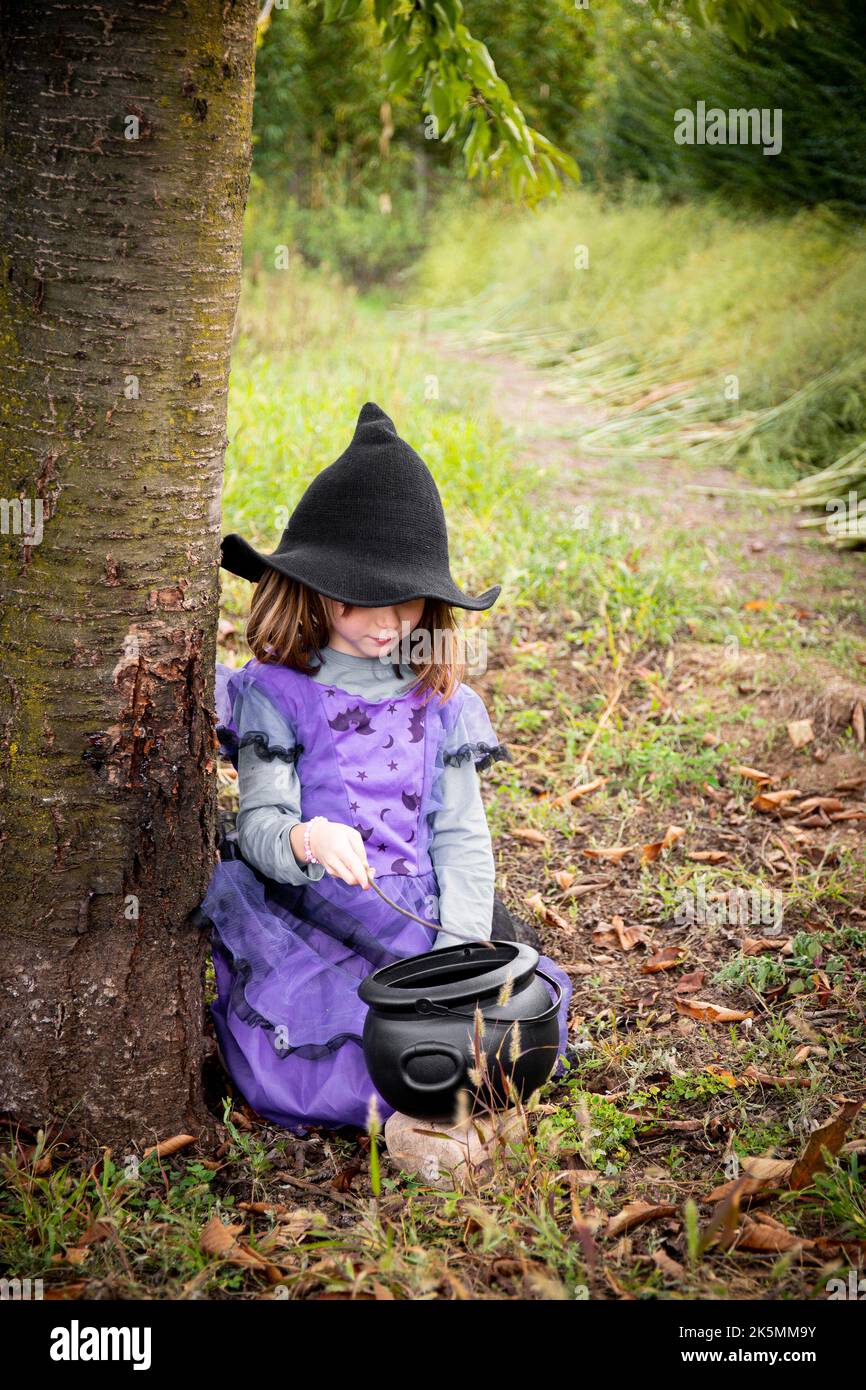 Enfant caucasien fille, 6 ans, en costume de sorcière violet halloween et chapeau noir, jouant à l'extérieur avec un chou-fleur. Tir vertical. Banque D'Images