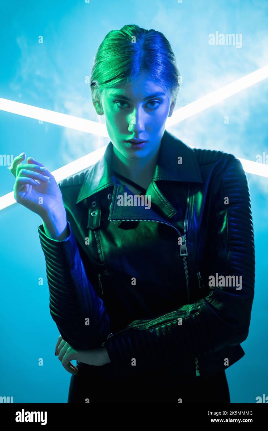 La mode cyberpunk. Lumière de néon personnes. Style urbain futuriste. Bleu vert portrait couleur de la femme arrogante en cuir noir veste sur blanc fumée LED l Banque D'Images