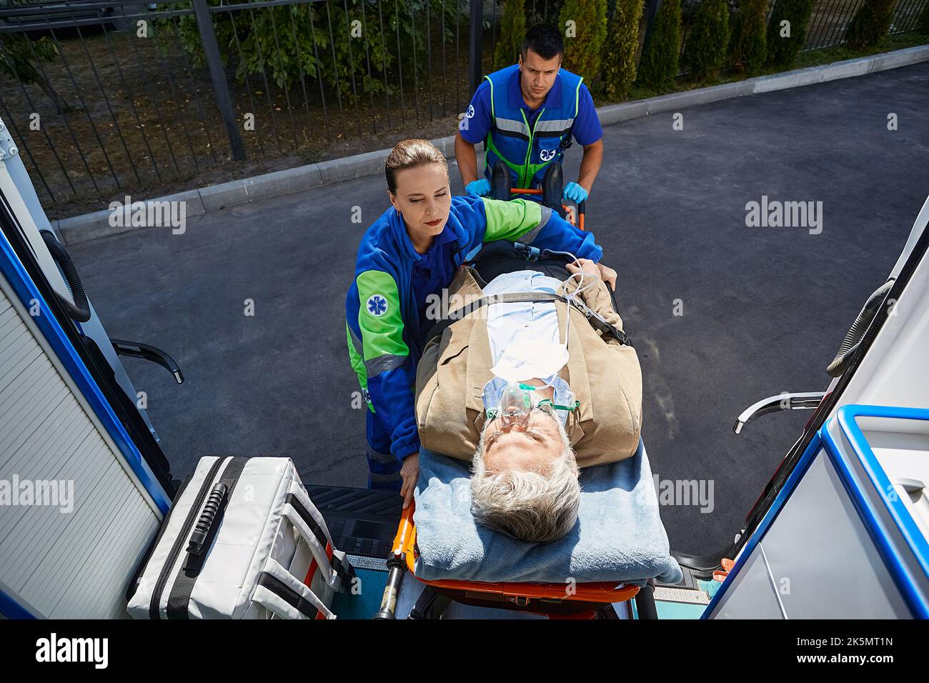 Les ambulanciers paramédicaux chargent un homme âgé avec un masque respiratoire dans une ambulance sur un brancard médical. Traitement d'urgence, EMS Banque D'Images