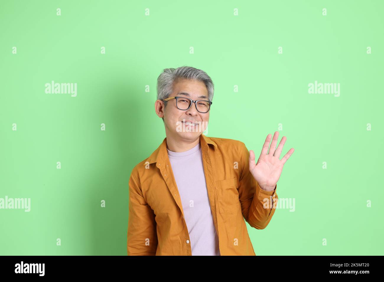 L'homme asiatique de 40s adultes avec une chemise jaune sur fond vert. Banque D'Images