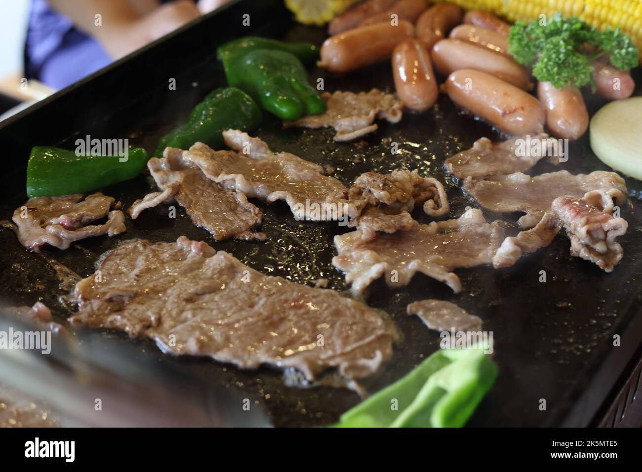 C'est une photo d'un plat de barbecue de style japonais. Sur la plaque de cuisson, il y a du porc, des poivrons verts, des saucisses et des pommes de terre. Banque D'Images