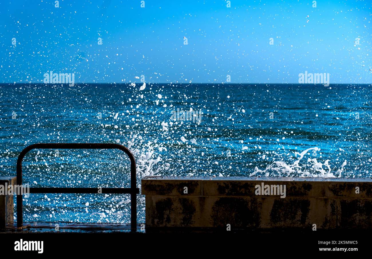 Des vagues bleues se sont écrasée contre la jetée, créant une explosion de mousse blanche lors d'un après-midi ensoleillé Banque D'Images