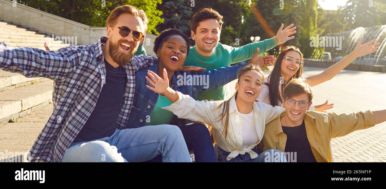 De jeunes amis heureux et joyeux posant pour une photo de groupe dans un parc d'été assis sur des marches. Banque D'Images