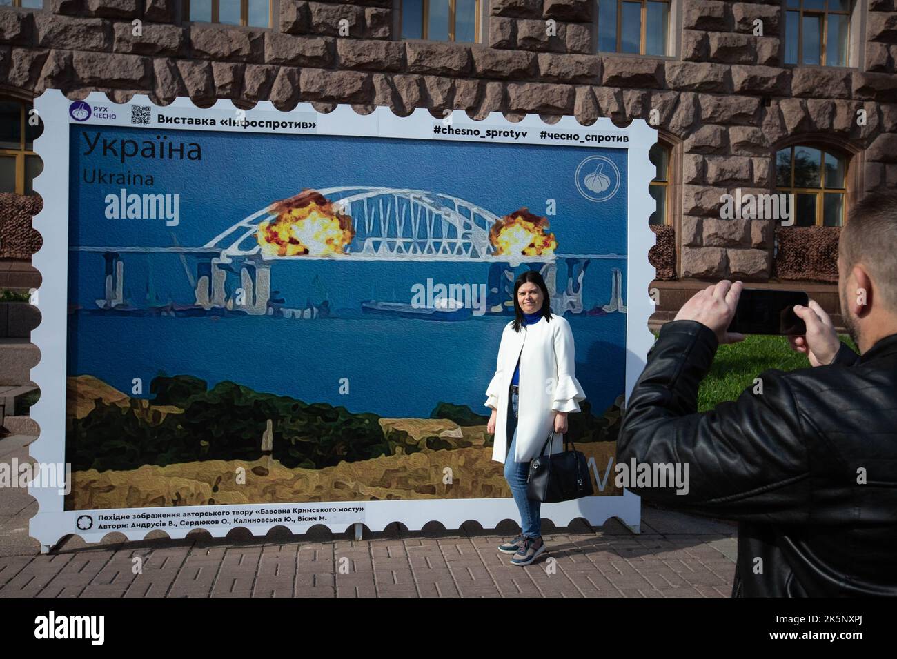 Kiev, Ukraine. 09th octobre 2022. Un homme prend une photo d'une femme avec un modèle de timbre représentant le pont de Crimée en feu en arrière-plan, dans le centre de Kiev. Sur 8 octobre, une explosion s'est produite sur le pont de Crimée construit par la Russie reliant la Russie à la péninsule de Crimée occupée par lui, endommageant une partie de la structure du pont. (Photo par Oleksii Chumachenko/SOPA Images/Sipa USA) crédit: SIPA USA/Alay Live News Banque D'Images