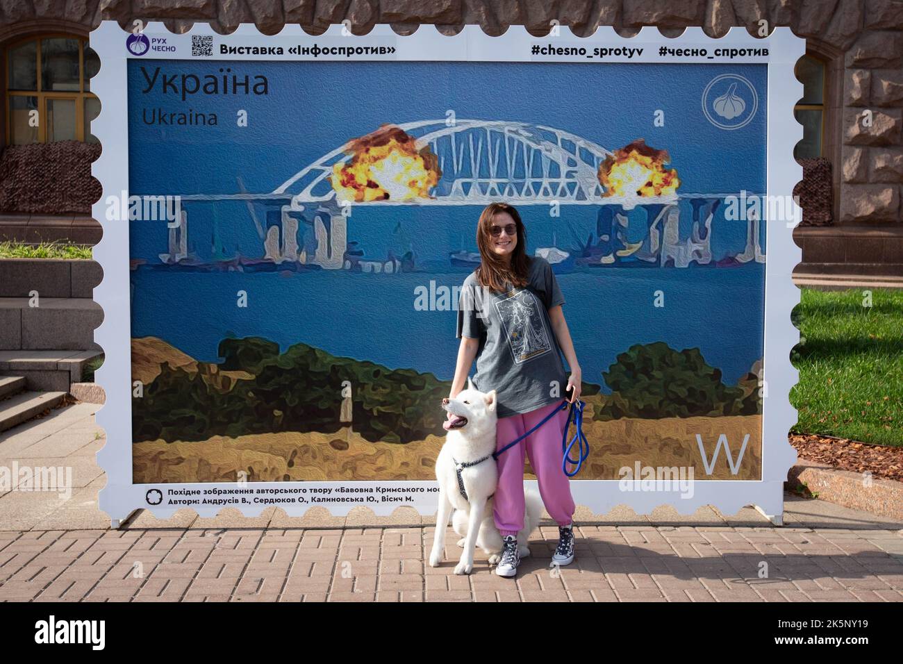 Kiev, Ukraine. 09th octobre 2022. Une femme avec un chien pose avec un modèle de timbre représentant le pont de Crimée en feu en arrière-plan, dans le centre de Kiev. Sur 8 octobre, une explosion s'est produite sur le pont de Crimée construit par la Russie reliant la Russie à la péninsule de Crimée occupée par lui, endommageant une partie de la structure du pont. (Photo par Oleksii Chumachenko/SOPA Images/Sipa USA) crédit: SIPA USA/Alay Live News Banque D'Images